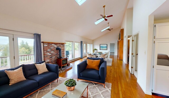 living room featuring a skylight, high vaulted ceiling, light hardwood / wood-style flooring, a wood stove, and ceiling fan