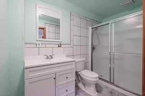 bathroom featuring vanity, toilet, walk in shower, and tile walls