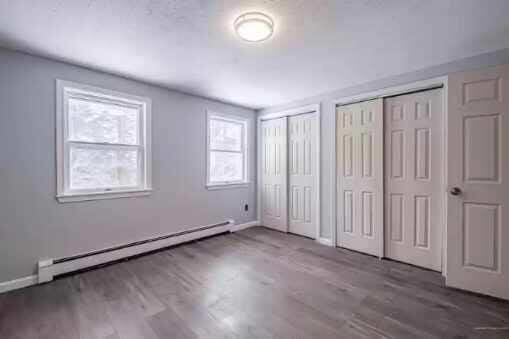 unfurnished bedroom with wood-type flooring, multiple closets, and a baseboard radiator