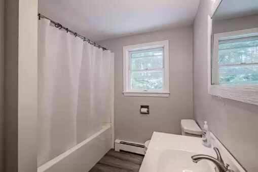 bathroom featuring sink, shower / bathtub combination with curtain, a baseboard radiator, and hardwood / wood-style flooring