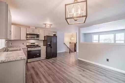 kitchen with sink, appliances with stainless steel finishes, decorative light fixtures, light stone counters, and wood-type flooring