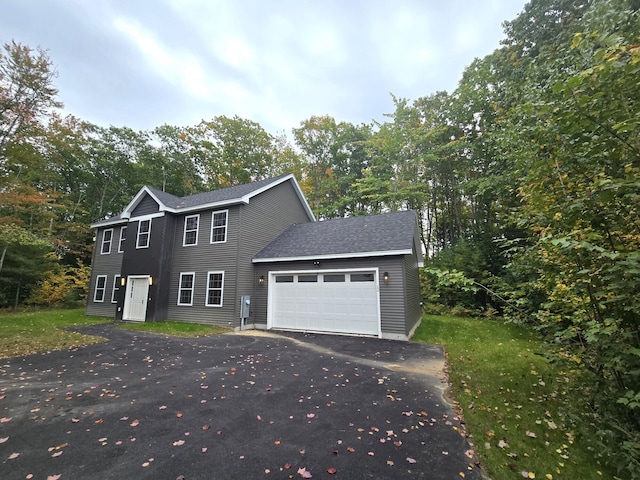 colonial inspired home with an attached garage, a shingled roof, and aphalt driveway