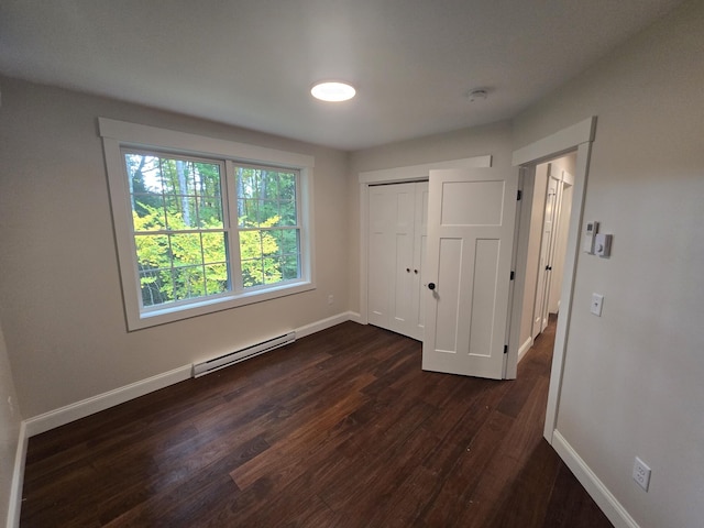unfurnished bedroom featuring a closet, baseboards, a baseboard heating unit, and dark wood-type flooring