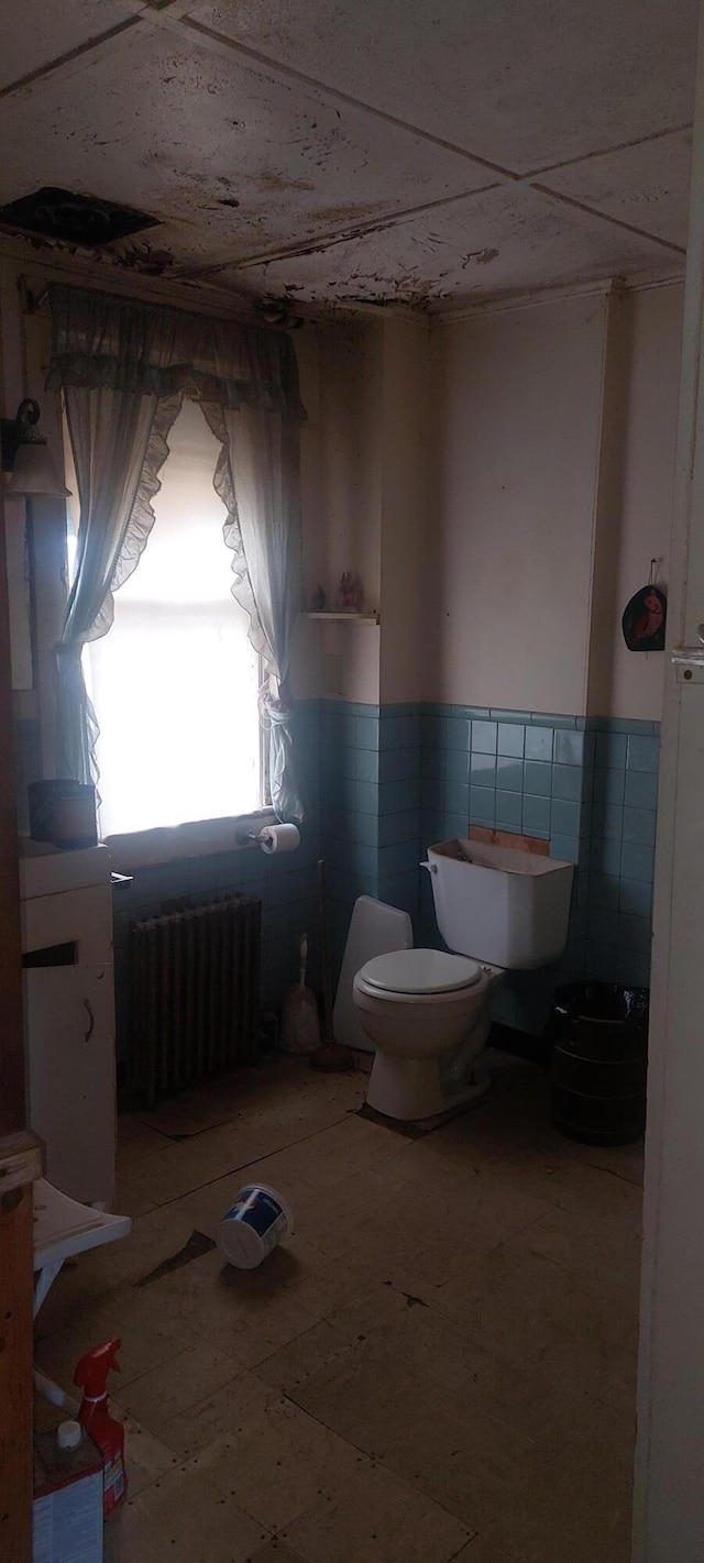 bathroom featuring radiator heating unit, toilet, and tile walls