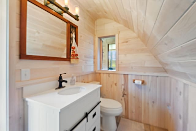 bathroom featuring toilet, lofted ceiling, wood walls, and vanity