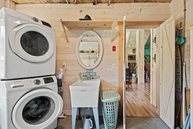 clothes washing area with stacked washing maching and dryer, wood walls, and sink