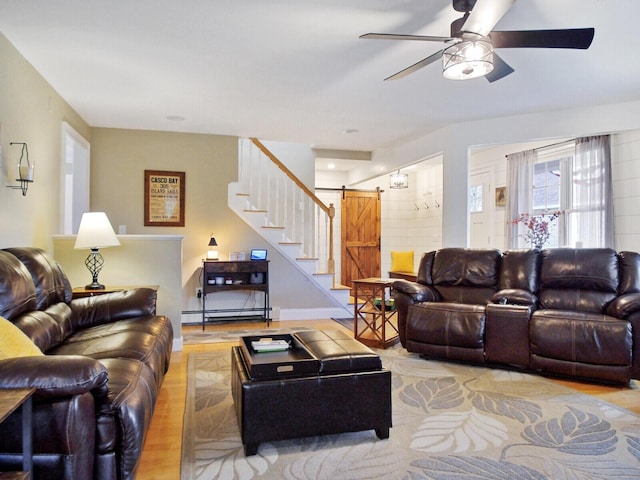 living room featuring ceiling fan, a barn door, light hardwood / wood-style floors, and baseboard heating