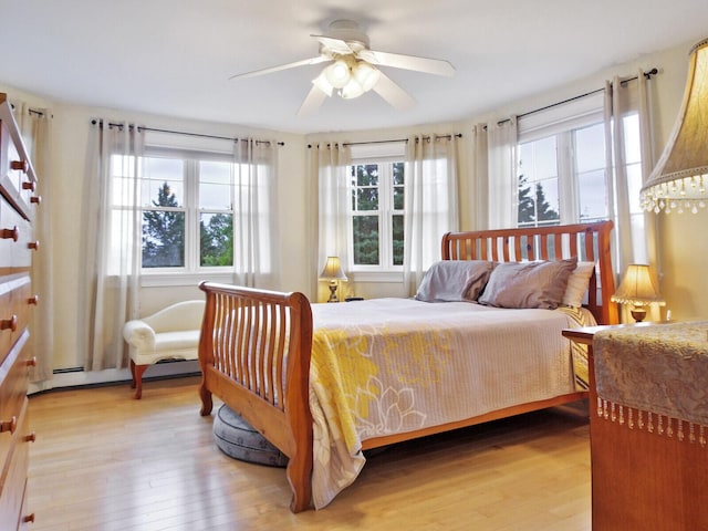 bedroom featuring ceiling fan, a baseboard heating unit, light wood-type flooring, and multiple windows