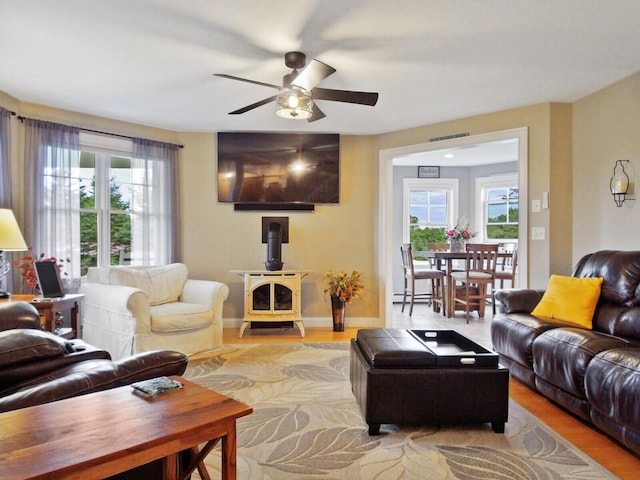 living room with a wood stove, light hardwood / wood-style flooring, baseboard heating, and ceiling fan