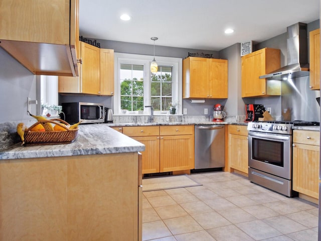 kitchen with wall chimney exhaust hood, light stone counters, decorative light fixtures, light brown cabinetry, and appliances with stainless steel finishes