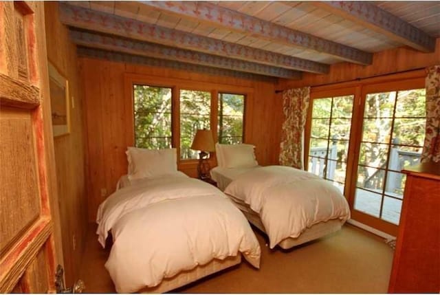 carpeted bedroom featuring beam ceiling, access to exterior, and wooden walls