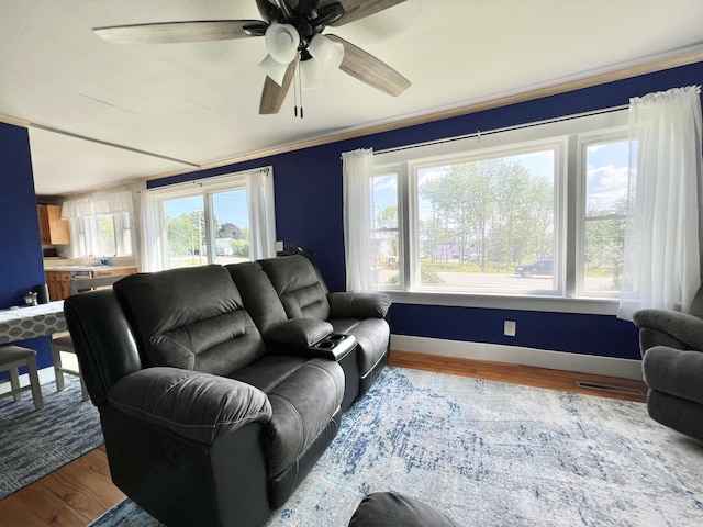 living area featuring a ceiling fan, a healthy amount of sunlight, baseboards, and wood finished floors