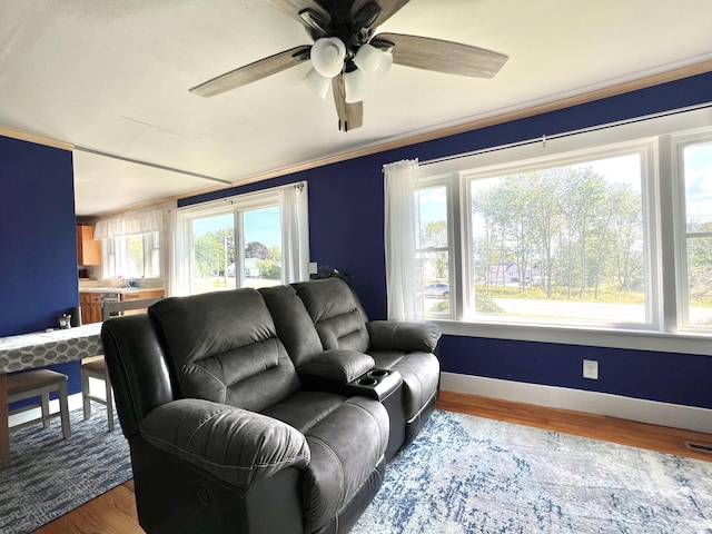 living area featuring ceiling fan, crown molding, baseboards, and wood finished floors