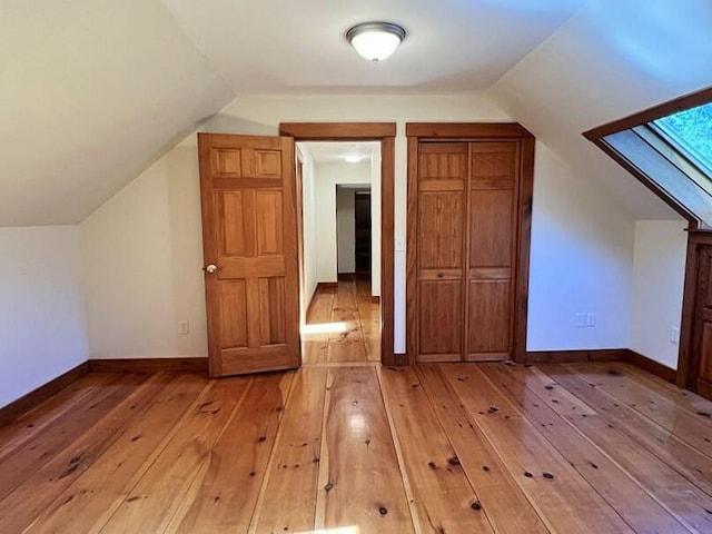 bonus room with vaulted ceiling with skylight and light wood-type flooring