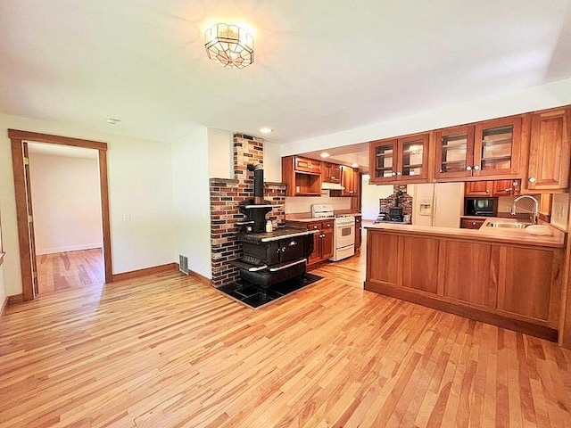 kitchen with light hardwood / wood-style floors, kitchen peninsula, sink, white appliances, and a wood stove