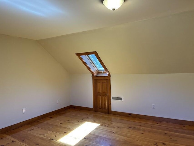 bonus room with vaulted ceiling with skylight and light hardwood / wood-style flooring