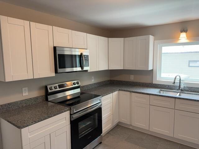 kitchen featuring dark stone countertops, stainless steel appliances, white cabinets, light tile patterned flooring, and sink