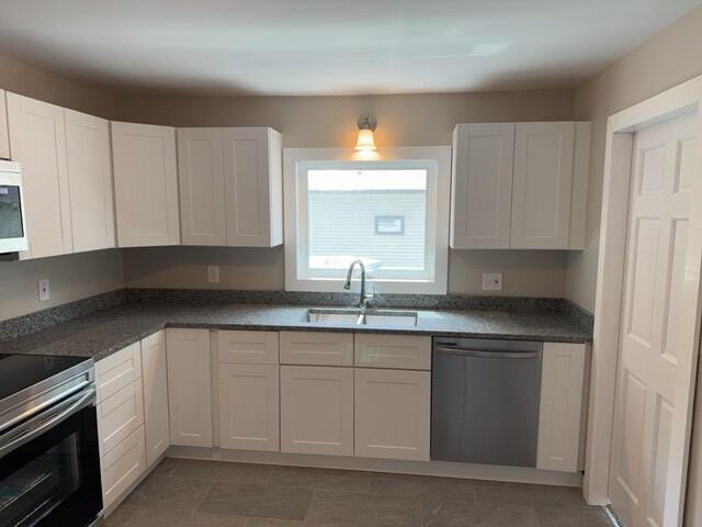 kitchen with stainless steel appliances, dark tile patterned floors, white cabinets, and sink