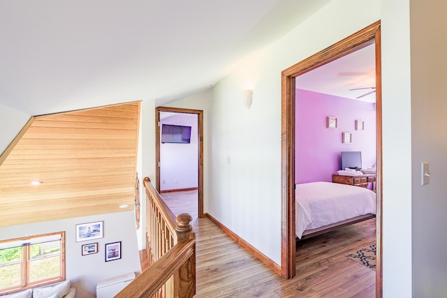 hall with light wood-type flooring, baseboards, lofted ceiling, and an upstairs landing