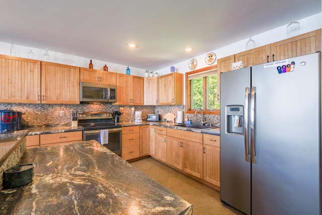 kitchen with appliances with stainless steel finishes, dark stone countertops, a sink, light brown cabinetry, and backsplash