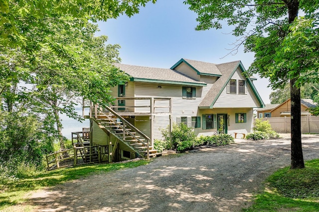 view of front of house with driveway, stairway, roof with shingles, fence, and a deck