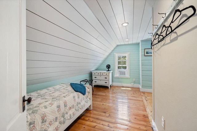 bedroom featuring wood walls, light hardwood / wood-style floors, and vaulted ceiling