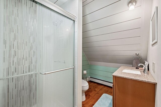 bathroom with an enclosed shower, vanity, baseboard heating, wood-type flooring, and toilet