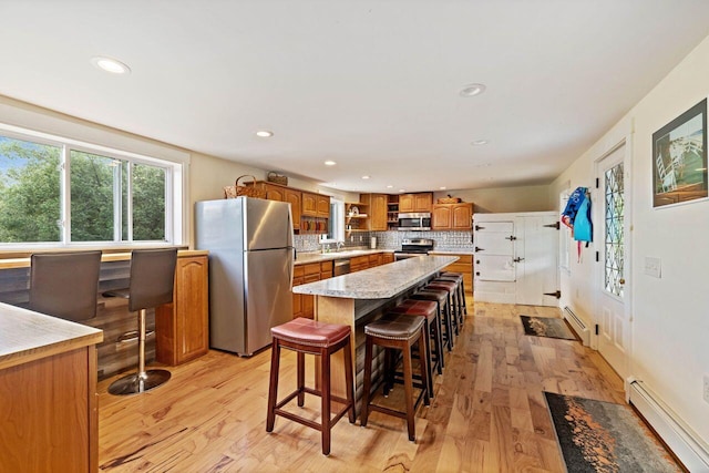 kitchen featuring appliances with stainless steel finishes, a kitchen island, a baseboard heating unit, and a breakfast bar area