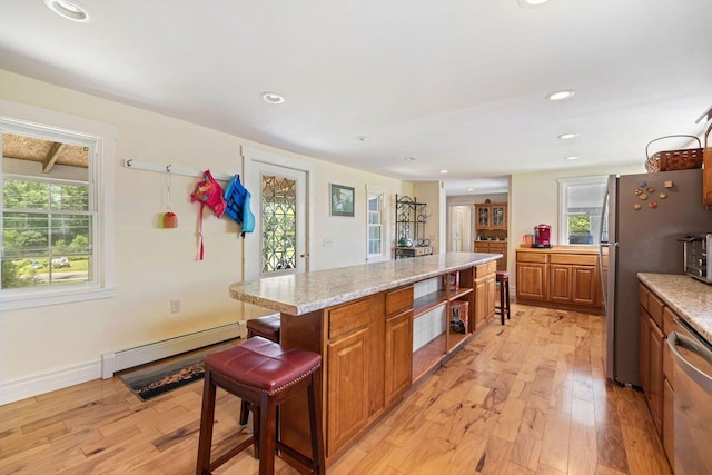 kitchen with light stone countertops, a baseboard heating unit, light hardwood / wood-style flooring, a kitchen island, and fridge