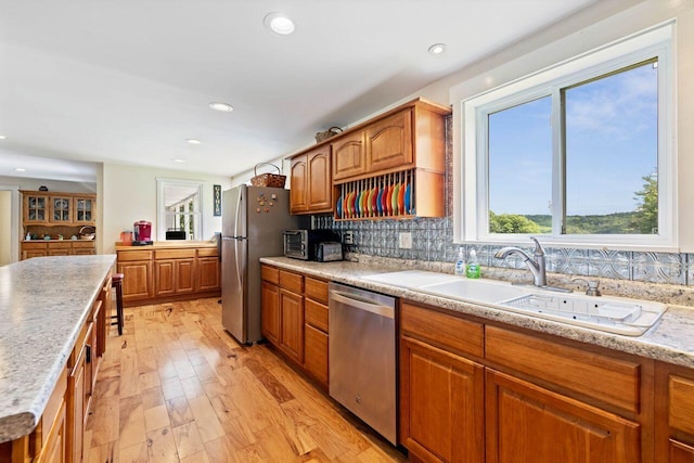 kitchen with decorative backsplash, light wood-type flooring, sink, and appliances with stainless steel finishes