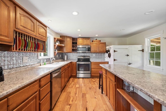 kitchen with plenty of natural light, backsplash, appliances with stainless steel finishes, and light hardwood / wood-style flooring