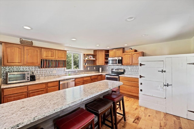 kitchen featuring light stone countertops, appliances with stainless steel finishes, a breakfast bar, sink, and light hardwood / wood-style flooring