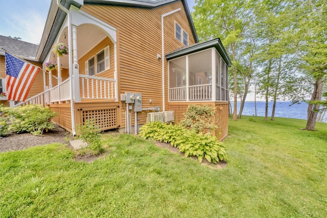 rear view of house featuring a water view, a lawn, and a sunroom