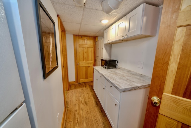 kitchen featuring light hardwood / wood-style flooring, a drop ceiling, and white cabinets