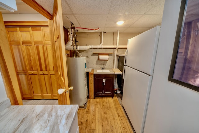 kitchen featuring white fridge, electric water heater, a paneled ceiling, light hardwood / wood-style flooring, and sink