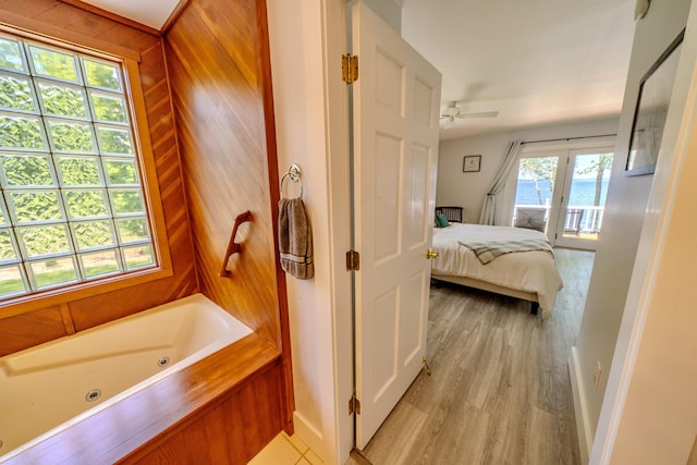 bathroom featuring hardwood / wood-style flooring, wooden walls, ceiling fan, a tub to relax in, and a water view