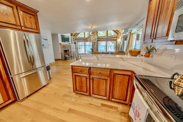 kitchen with stainless steel appliances, a fireplace, kitchen peninsula, a chandelier, and light wood-type flooring