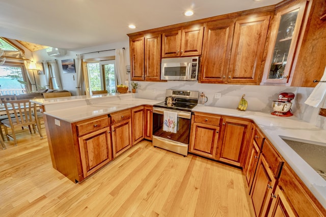 kitchen featuring light wood-type flooring, stainless steel appliances, a wall mounted AC, and kitchen peninsula