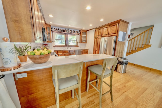 kitchen featuring kitchen peninsula, appliances with stainless steel finishes, light wood-type flooring, a kitchen breakfast bar, and sink