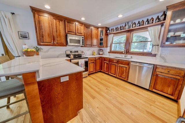 kitchen with kitchen peninsula, a kitchen bar, sink, light hardwood / wood-style flooring, and appliances with stainless steel finishes