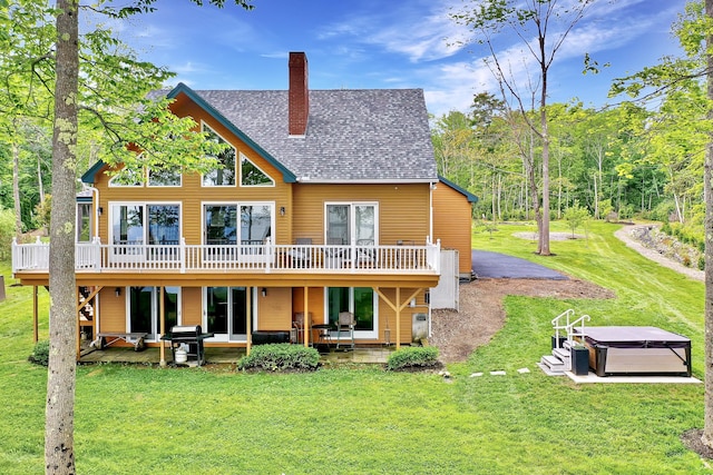 rear view of property with a deck, a patio area, a hot tub, and a yard