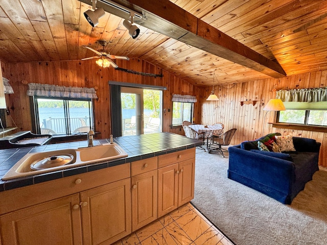 kitchen with tile counters, lofted ceiling with beams, sink, and wood walls