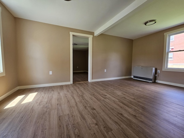 unfurnished living room featuring beamed ceiling, hardwood / wood-style floors, radiator, and heating unit