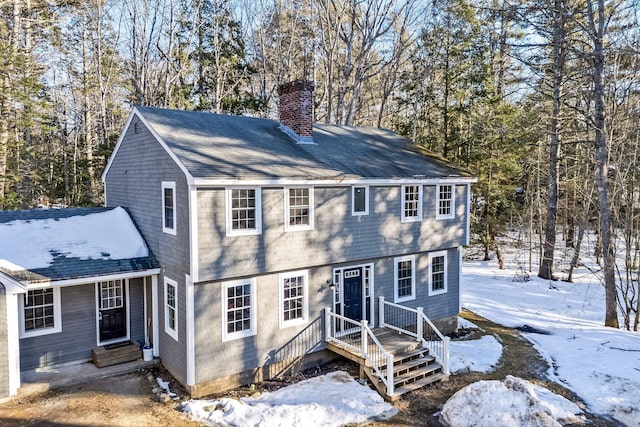 colonial house featuring a chimney and a shingled roof