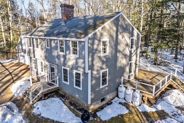 view of snow covered exterior with a wooden deck, roof with shingles, and a chimney