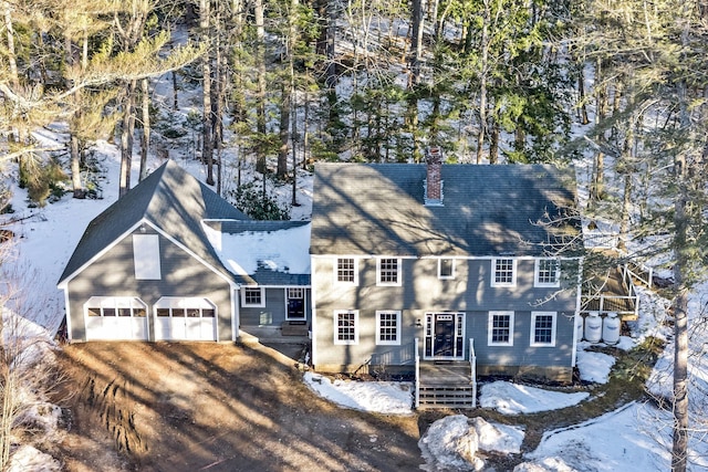 view of front of house featuring an attached garage, dirt driveway, and a chimney