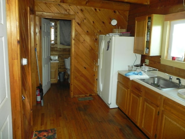 kitchen featuring dark hardwood / wood-style flooring, sink, wood walls, and white fridge with ice dispenser