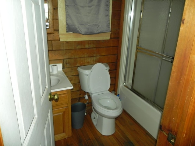 full bathroom featuring toilet, vanity, combined bath / shower with glass door, wood-type flooring, and wooden walls