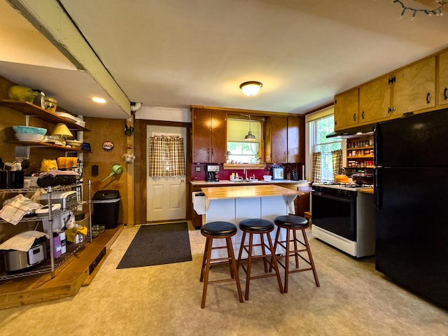 kitchen featuring black refrigerator, white gas range, a kitchen breakfast bar, and a center island