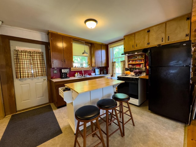 kitchen with a kitchen island, sink, a kitchen bar, gas range gas stove, and black fridge